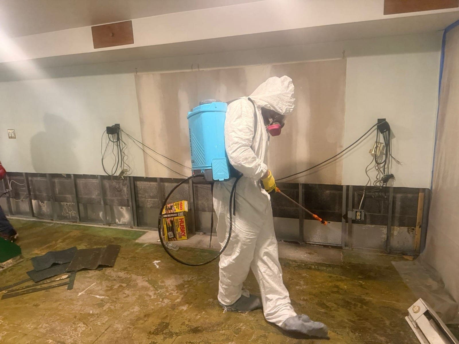 Technician in full protective gear spraying antimicrobial treatment on flood-cut basement walls