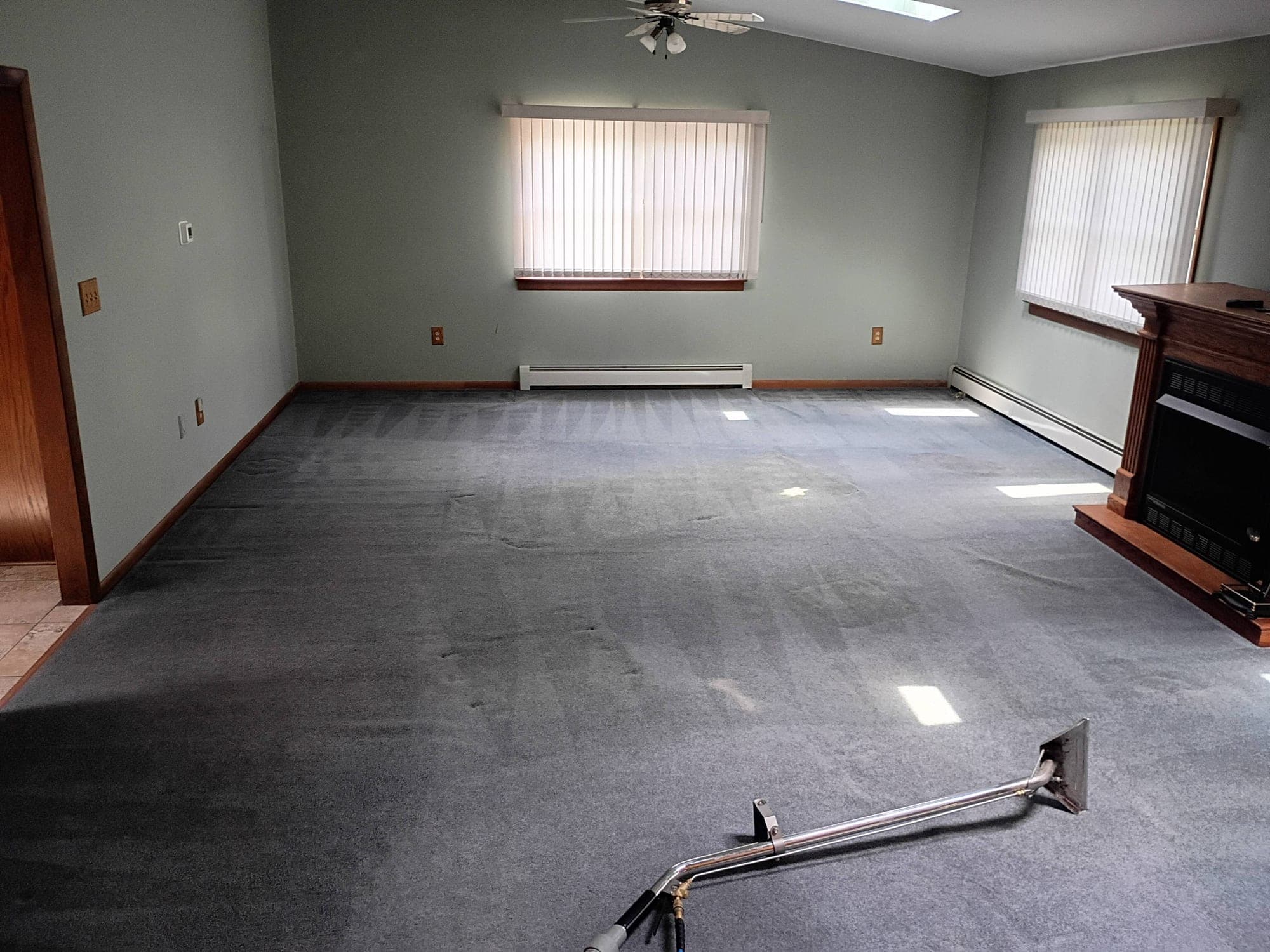 Carpet cleaning wand in action in a spacious living room with fireplace and skylight