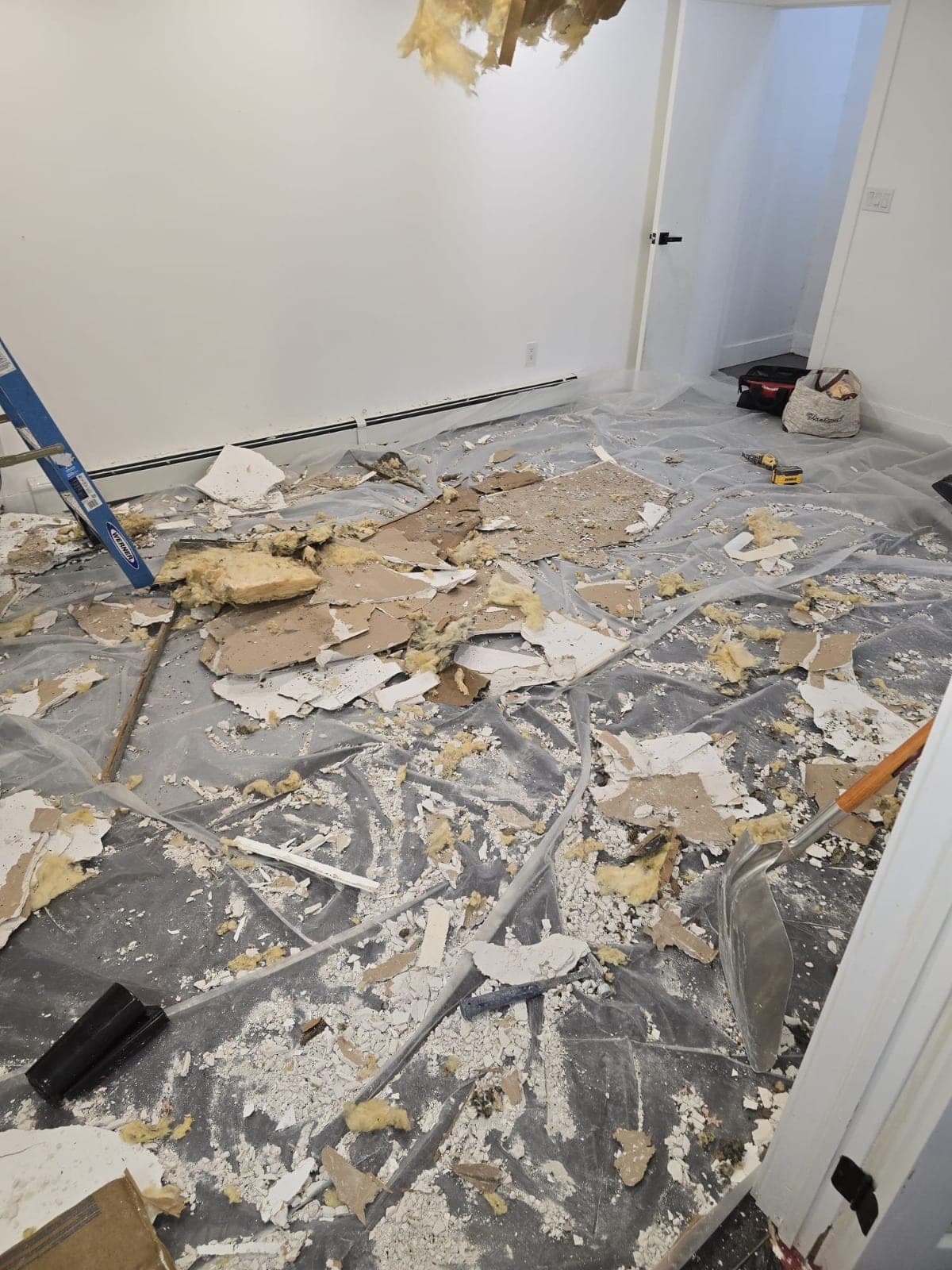 Water-damaged ceiling drywall and wet insulation removed onto a protected bedroom floor