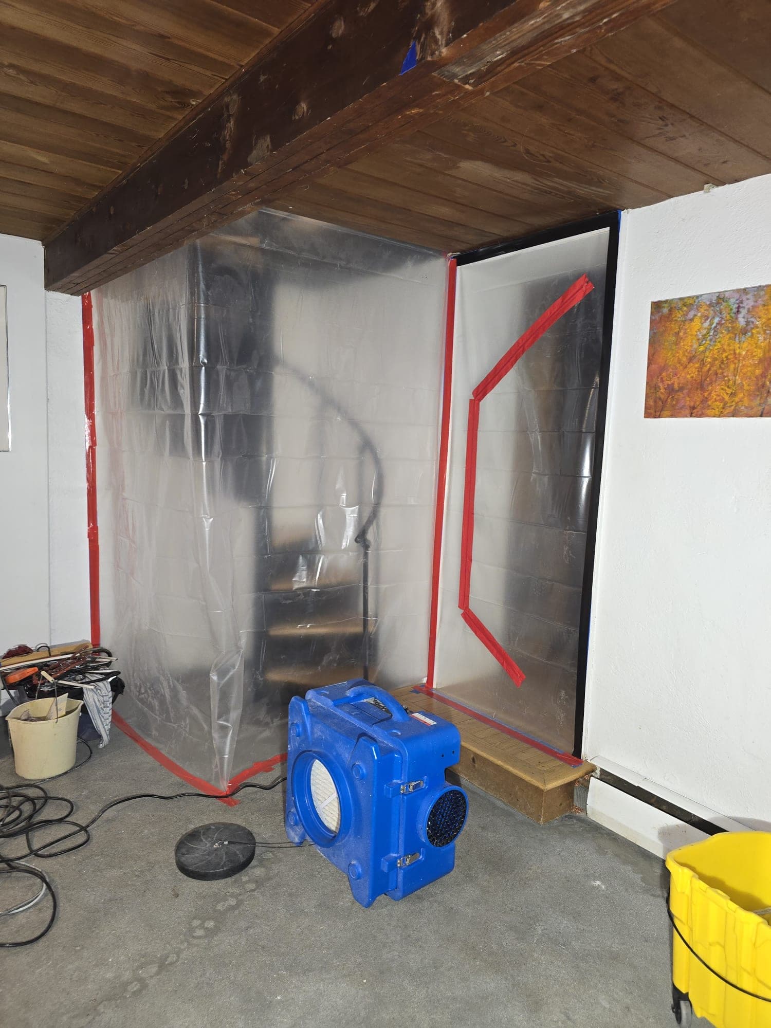 Basement stairwell wrapped in poly containment with a HEPA air scrubber at the opening