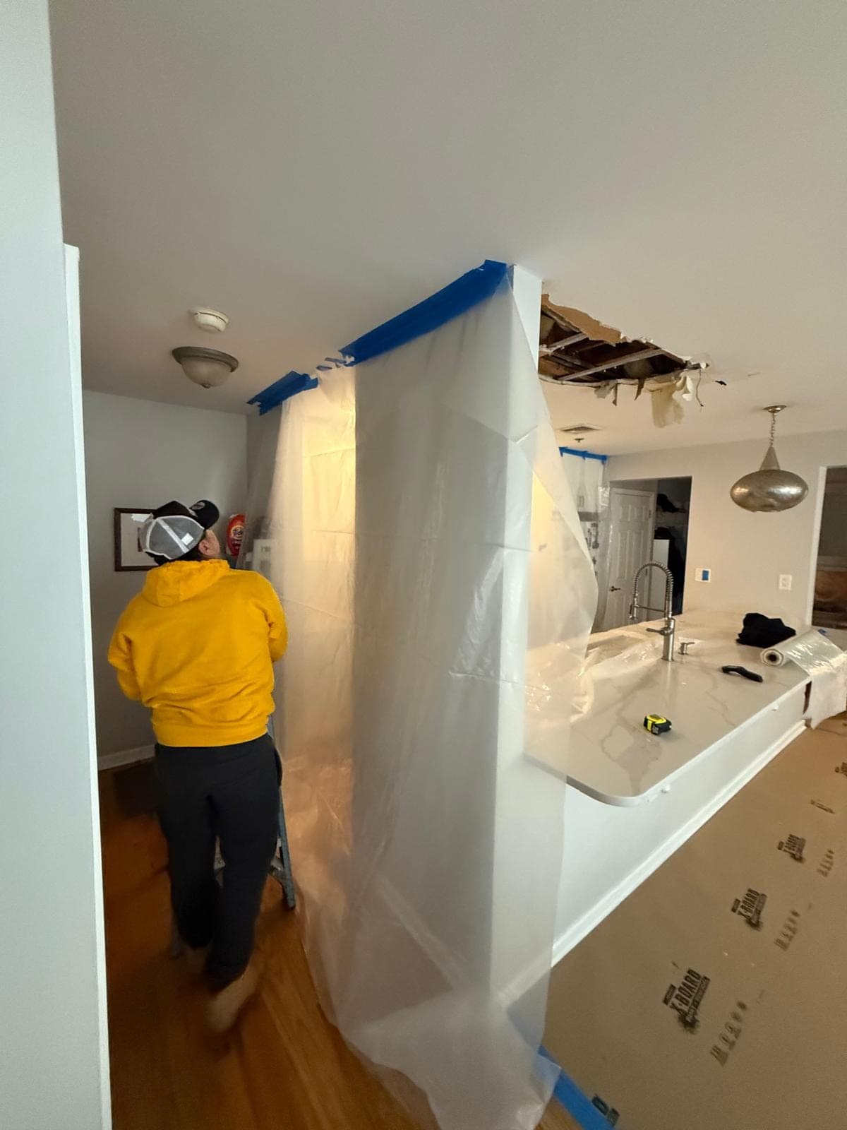 Poly containment wall built beside a kitchen island below a water-damaged ceiling opening