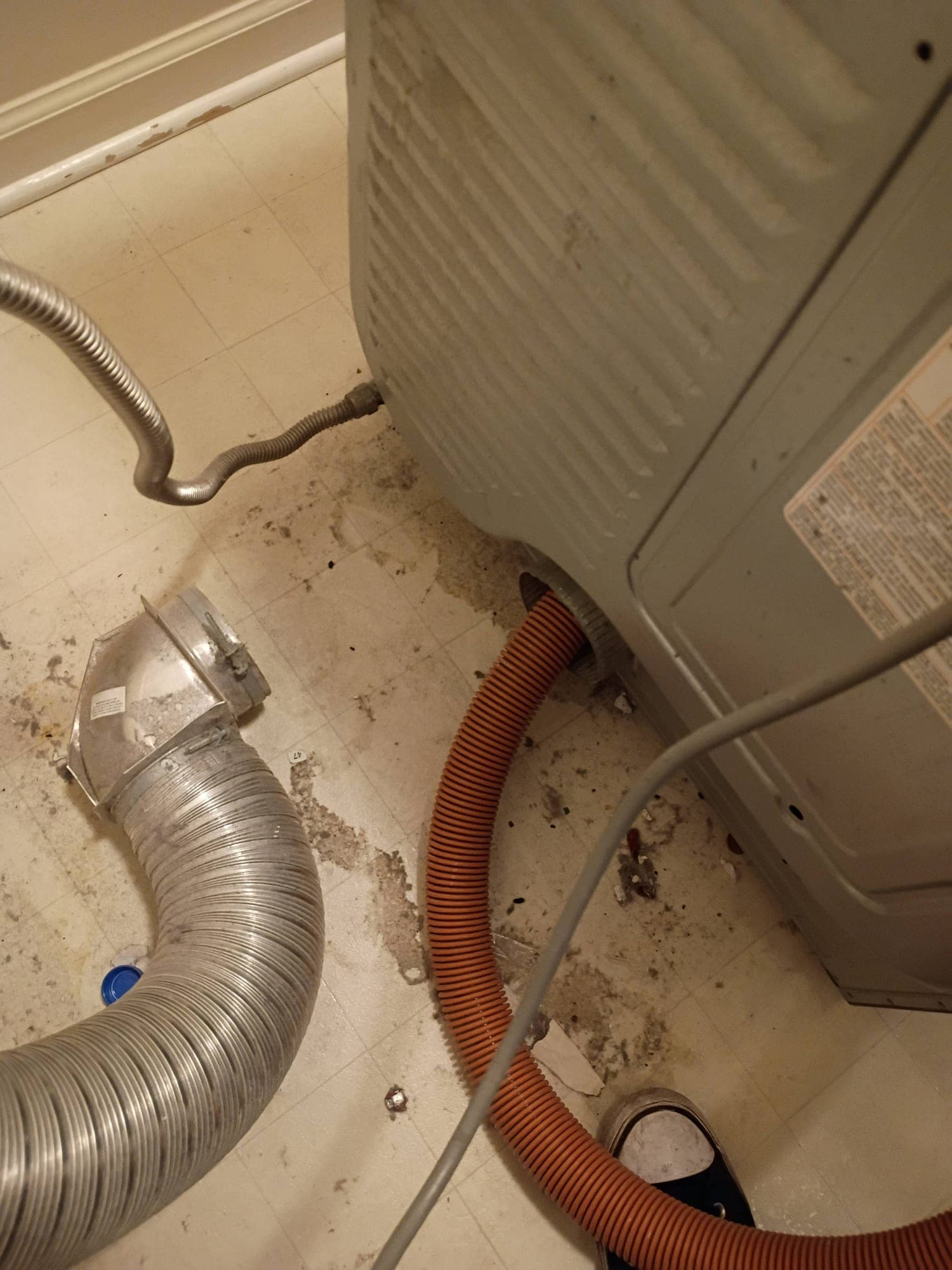 Disconnected dryer vent hose on a lint-covered laundry room floor