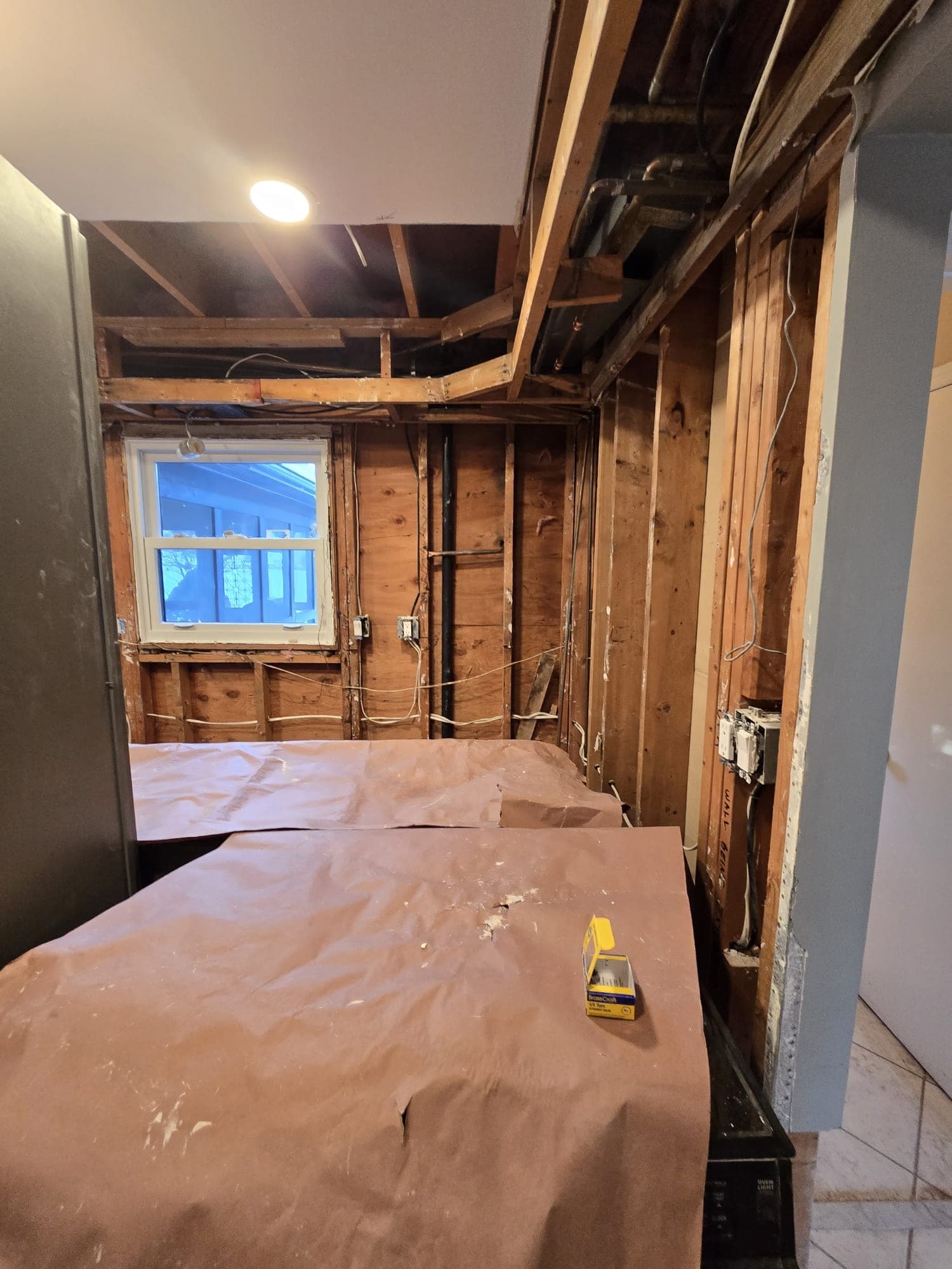 Kitchen gutted to bare studs and open ceiling joists after water damage, appliances protected
