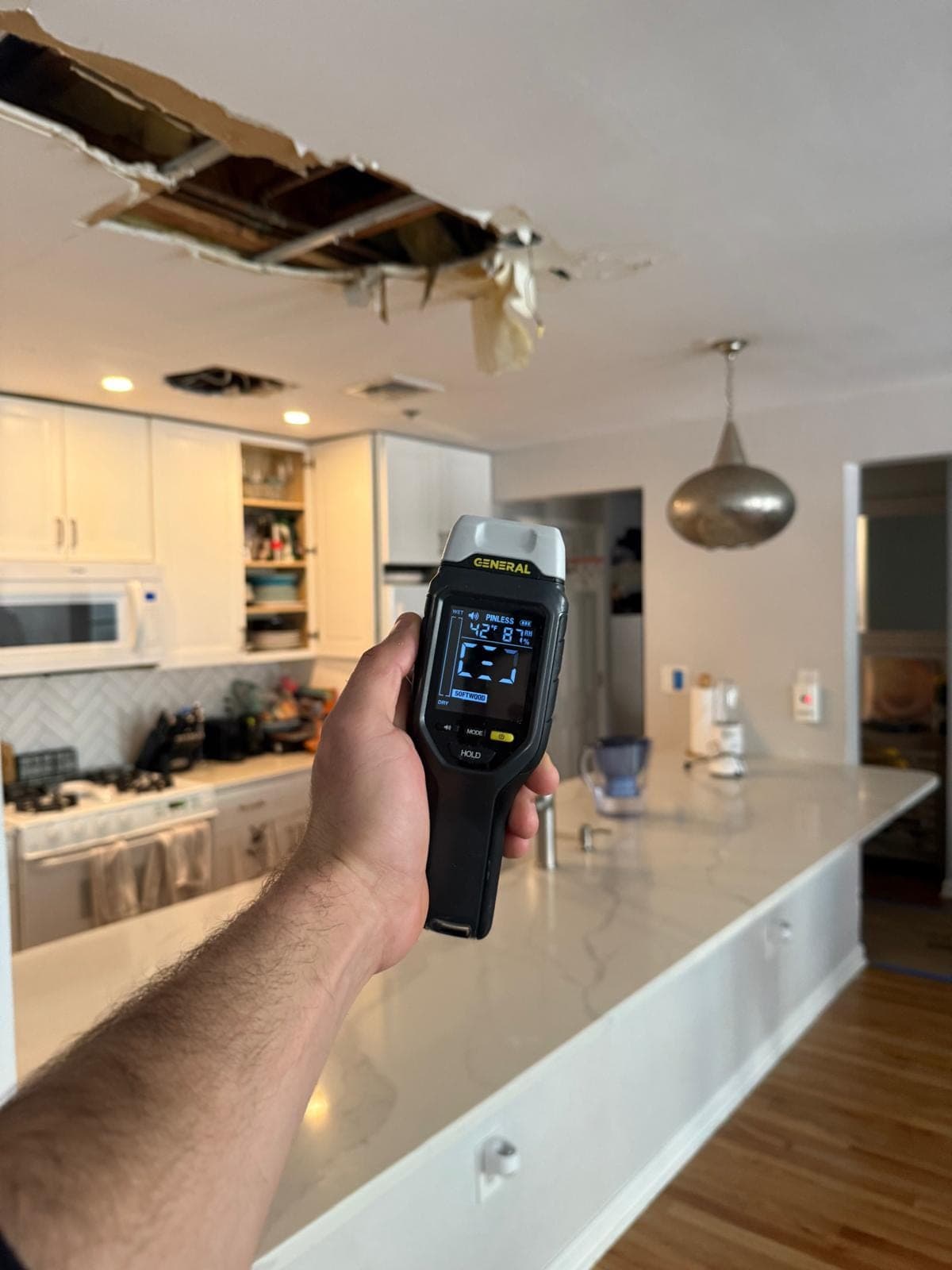 Moisture meter reading taken in front of a collapsed water-damaged kitchen ceiling